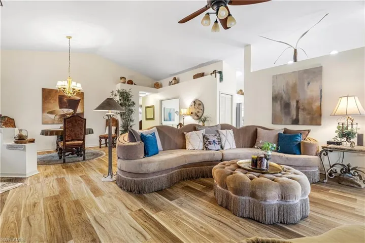 Living room featuring lofted ceiling, light wood-type flooring, and ceiling fan with notable chandelier