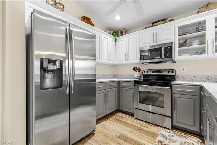 Kitchen with appliances with stainless steel finishes, lofted ceiling, white cabinetry, light wood-type flooring, and gray cabinetry