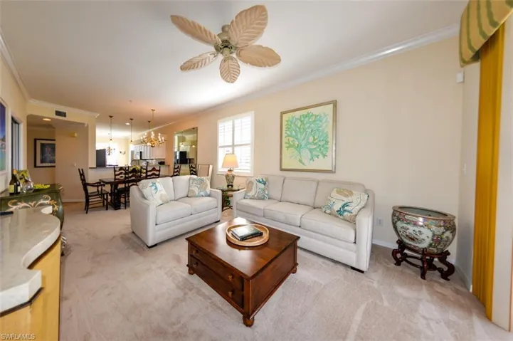 Living room with light carpet, ornamental molding, and ceiling fan with notable chandelier