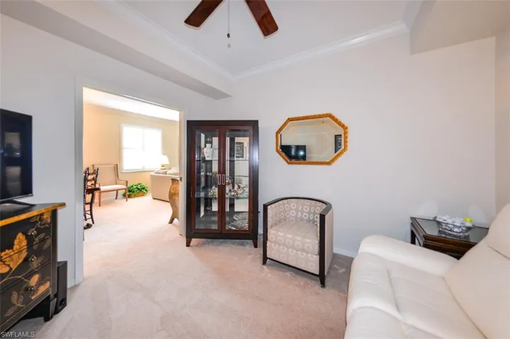 Carpeted living room with ceiling fan and crown molding