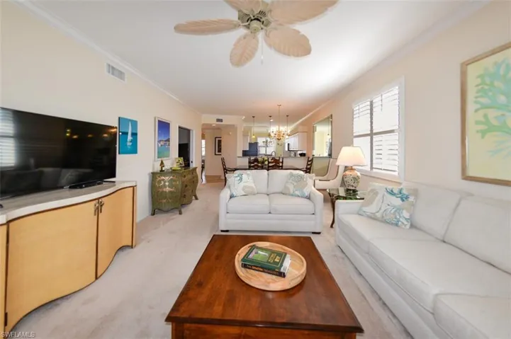 Carpeted living room featuring ornamental molding and ceiling fan with notable chandelier