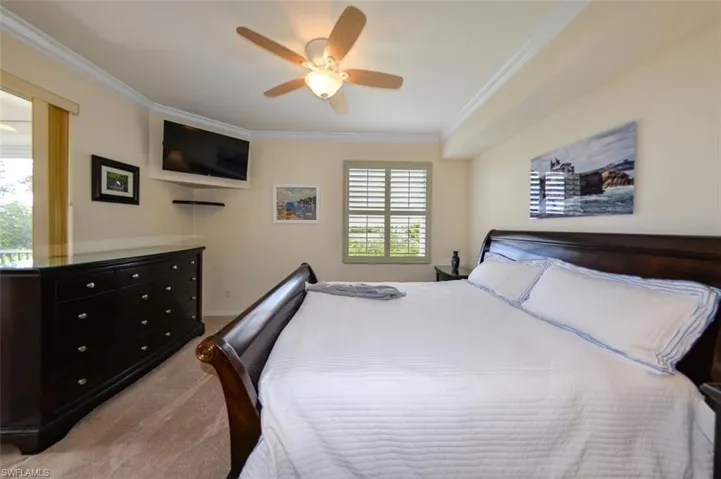 Carpeted bedroom with ceiling fan, multiple windows, and crown molding
