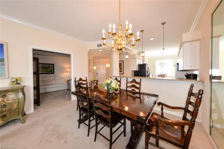 Dining space featuring a notable chandelier, crown molding, and light colored carpet