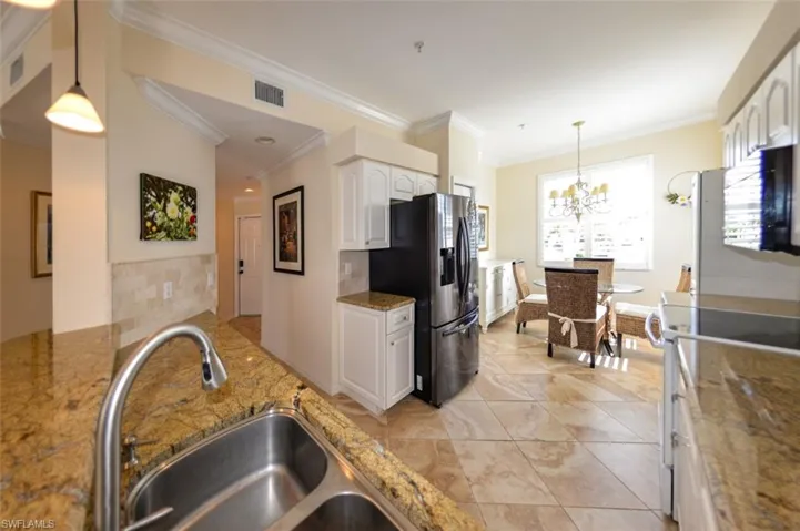 Kitchen with white cabinetry, backsplash, stainless steel fridge, and crown molding