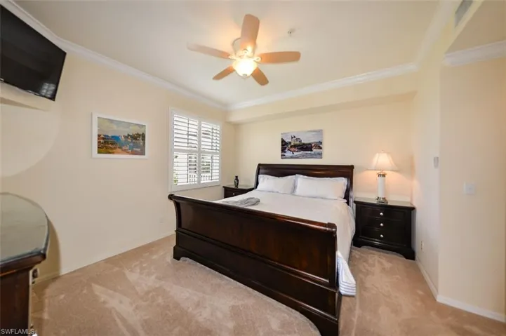 Carpeted bedroom with ceiling fan and crown molding