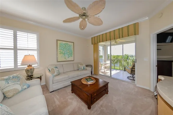 Carpeted living room featuring ceiling fan, crown molding, and a wealth of natural light