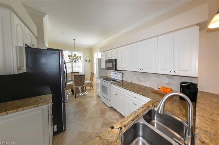 Kitchen featuring white cabinetry, black appliances, decorative light fixtures, sink, and tasteful backsplash