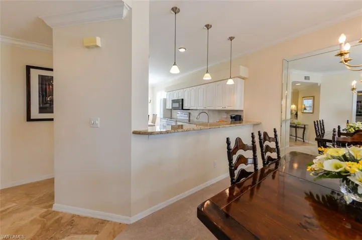 Kitchen with decorative light fixtures, light stone counters, white cabinetry, and crown molding