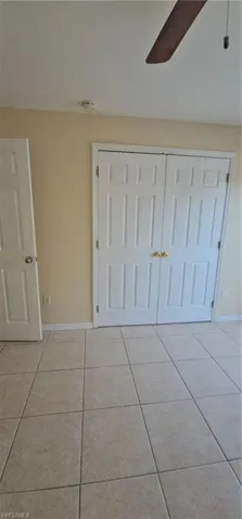 Unfurnished bedroom with light tile patterned floors, a closet, baseboards, and ceiling fan