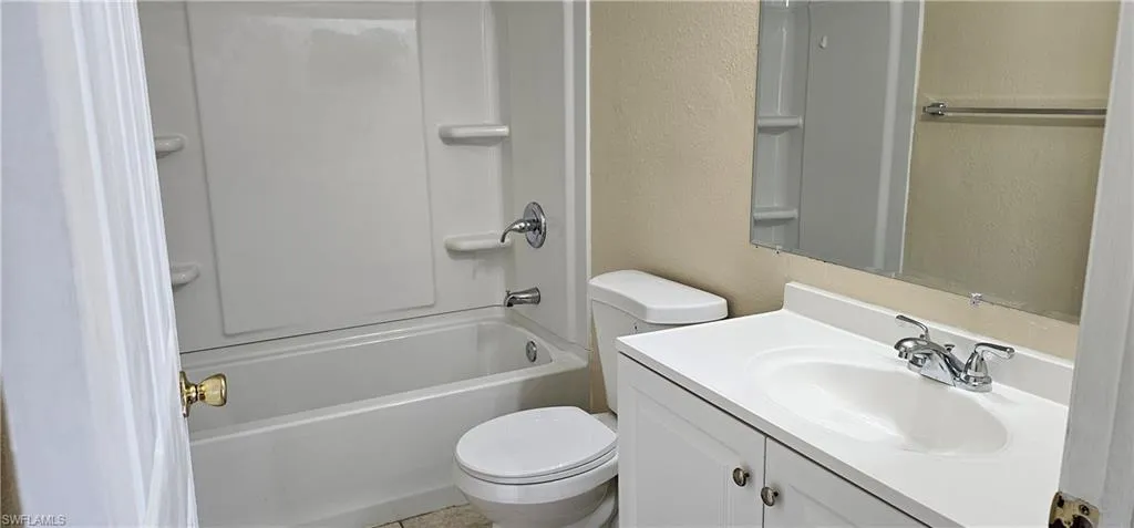 Bathroom featuring a textured wall, vanity, toilet, and shower / bathtub combination