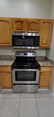 Kitchen featuring stainless steel range with electric cooktop, light tile patterned floors, light stone counters, and brown cabinets