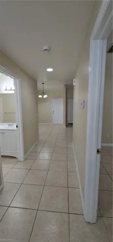 Hall featuring light tile patterned flooring, baseboards, a chandelier, and a sink