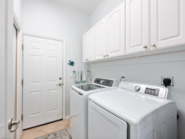 Laundry area featuring light tile patterned flooring, washing machine and dryer, and cabinets