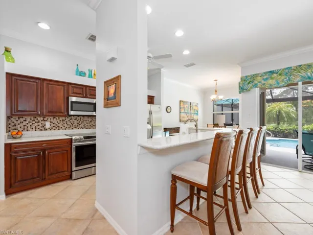 Kitchen featuring light tile patterned flooring, a breakfast bar area, tasteful backsplash, ceiling fan with notable chandelier, and appliances with stainless steel finishes