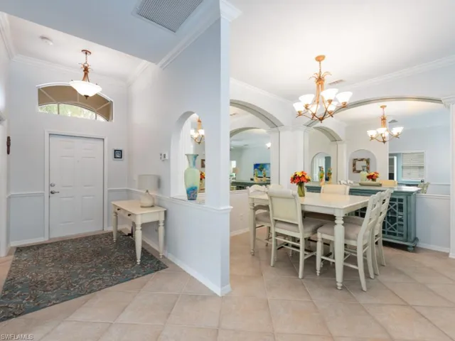 Tiled dining room featuring ornamental molding, decorative columns, and a chandelier