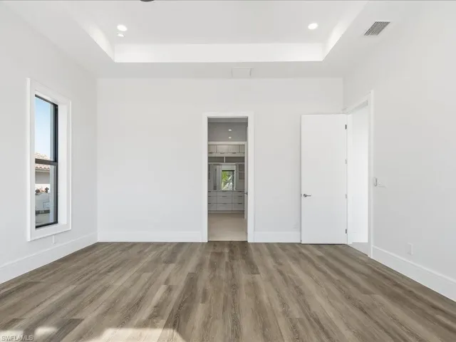 Unfurnished bedroom featuring a raised ceiling, light wood-style flooring, ensuite bathroom, and recessed lighting