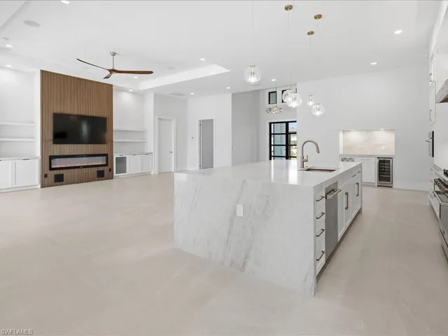 Kitchen featuring open floor plan, light stone countertops, a spacious island, white cabinets, and pendant lighting