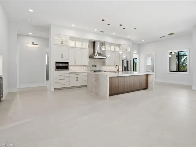 Kitchen with glass insert cabinets, white cabinets, a large island, hanging light fixtures, and recessed lighting
