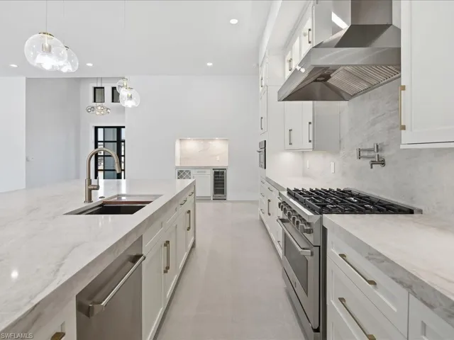 Kitchen featuring tasteful backsplash, stainless steel appliances, wall chimney range hood, light stone counters, and white cabinets