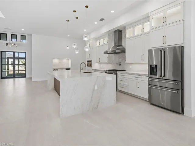 Kitchen with glass insert cabinets, premium appliances, wall chimney exhaust hood, tasteful backsplash, and light stone countertops