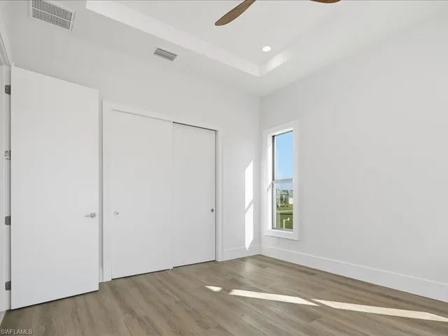 Unfurnished bedroom featuring wood finished floors, a closet, a tray ceiling, ceiling fan, and recessed lighting