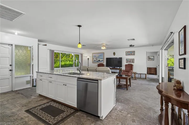 Kitchen featuring a kitchen island with sink, white cabinets, and dishwasher with pocketed doors leading out to the sparkling pool