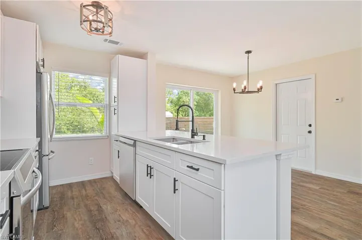 Kitchen featuring a sink, appliances with stainless steel finishes, dark wood-type flooring, a chandelier, and baseboards