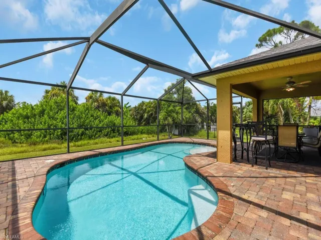View of pool with glass enclosure, a patio area, and ceiling fan