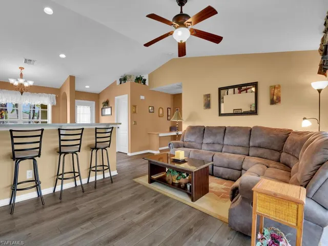 Living room with lofted ceiling, ceiling fan with notable chandelier, and hardwood / wood-style floors