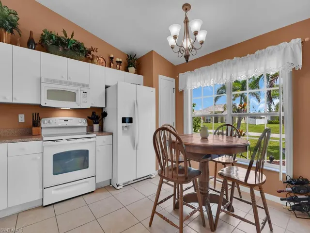 Kitchen with vaulted ceiling, an inviting chandelier, light tile flooring, white appliances, and pendant lighting