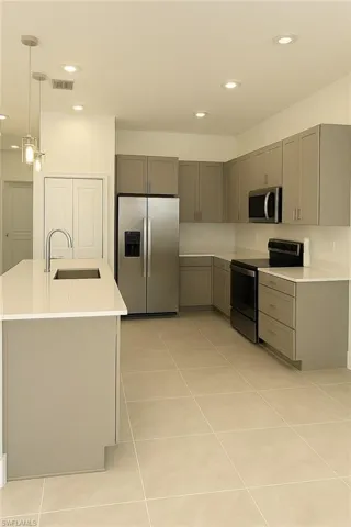 Kitchen with stainless steel appliances, gray cabinets, recessed lighting, an island with sink, and hanging light fixtures