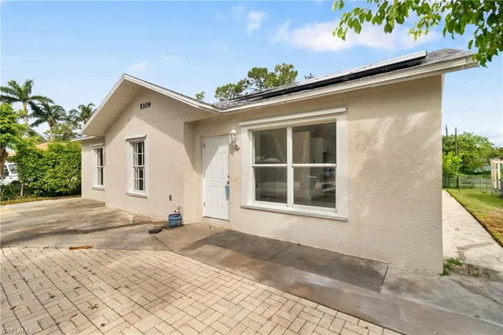 Back of property with stucco siding, roof mounted solar panels, and a patio