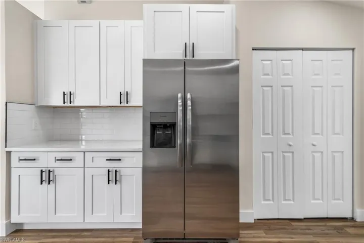 Kitchen featuring stainless steel refrigerator with ice dispenser, light countertops, wood finished floors, backsplash, and white cabinets