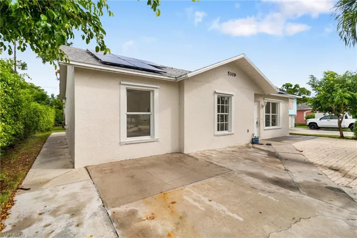 Rear view of house featuring solar panels, a shingled roof, and stucco siding