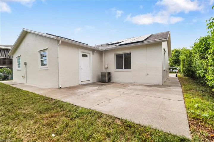 Rear view of property featuring stucco siding, roof mounted solar panels, a patio area, and a yard