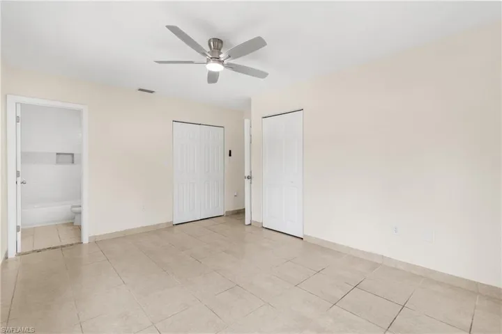 Unfurnished bedroom featuring light tile patterned flooring, connected bathroom, and a ceiling fan