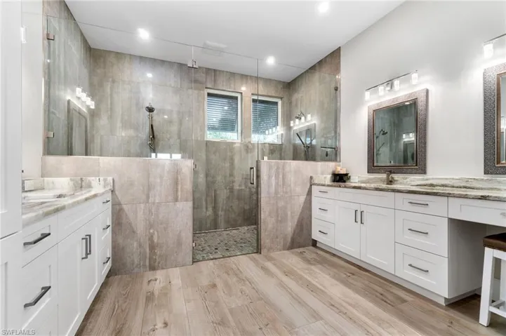Master bathroom featuring tile walls, a dual zone walk-in shower, glass shower door and dual vanity