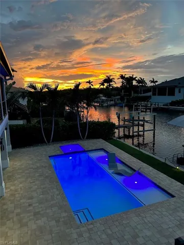 Pool at dusk featuring a patio and a water view