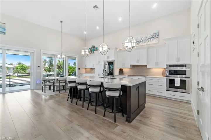 Kitchen with stainless steel double oven, plenty of natural light, an island with sink, and pendant lighting