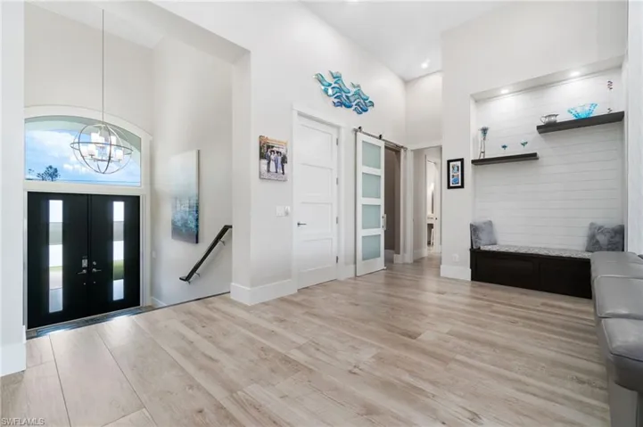 Entrance foyer with double custom doors, an inviting chandelier, a towering ceiling, and light wood-type flooring.