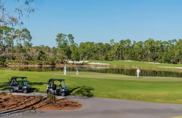 View of community featuring view of golf course, a yard, view of wooded area, and a water view