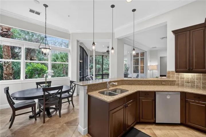 Kitchen with dark brown cabinetry, light stone countertops, decorative light fixtures, stainless steel dishwasher, and decorative backsplash