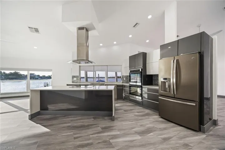 Kitchen with stainless steel appliances, a high ceiling, island range hood, recessed lighting, and modern cabinets