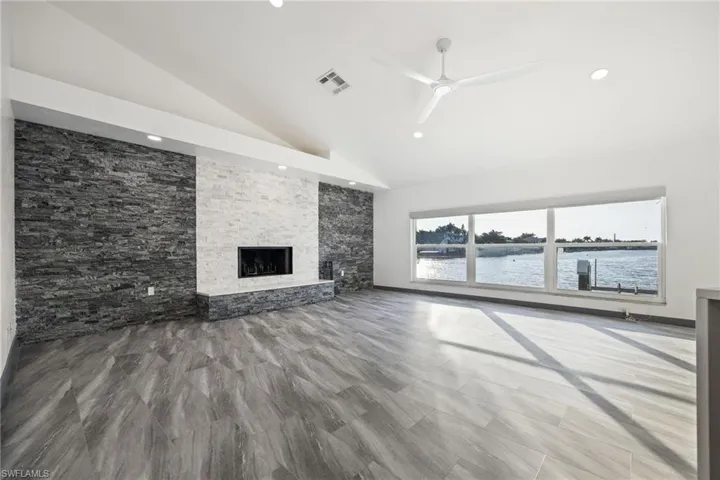 Unfurnished living room featuring a fireplace, ceiling fan, a water view, and high vaulted ceiling