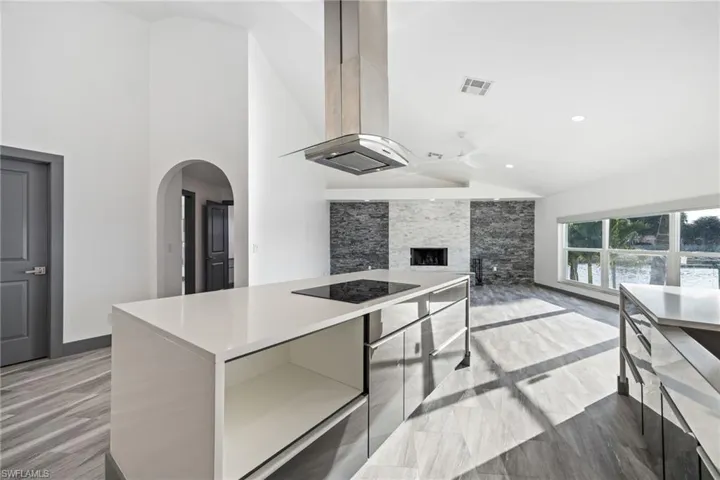 Kitchen featuring modern cabinets, island range hood, high vaulted ceiling, black electric cooktop, and arched walkways