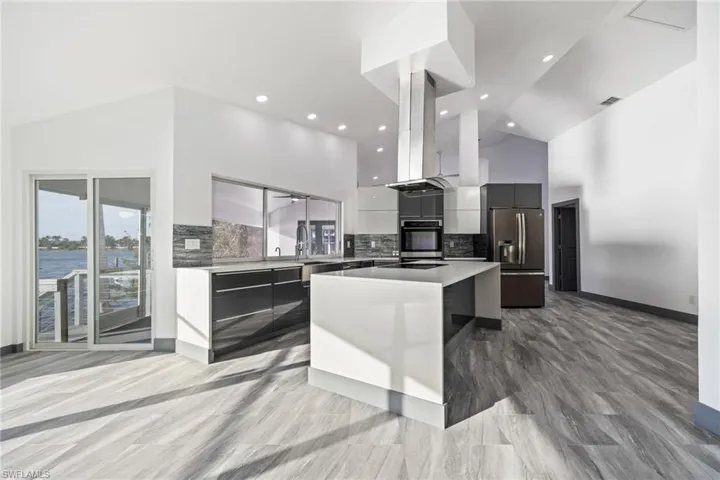 Kitchen featuring modern cabinets, stainless steel fridge with ice dispenser, a kitchen island, island range hood, and high vaulted ceiling