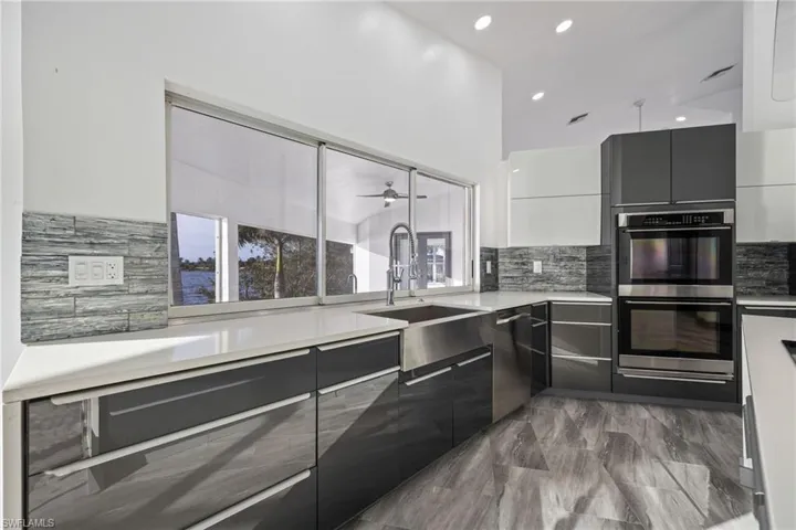 Kitchen with modern cabinets, stainless steel appliances, light stone counters, tasteful backsplash, and white cabinetry