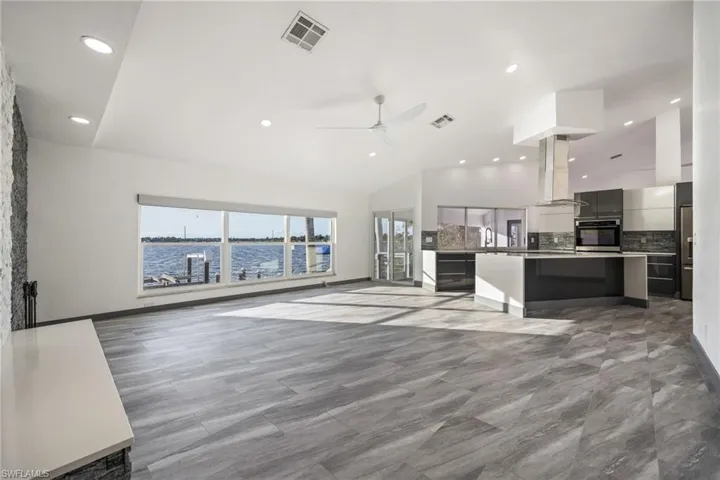 Unfurnished living room with lofted ceiling, ceiling fan, recessed lighting, and a water view