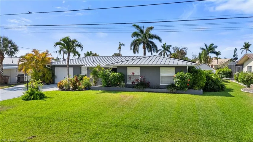 Ranch-style house featuring concrete driveway, a front lawn, an attached garage, stucco siding, and a standing seam roof  - Virtually Edited Image