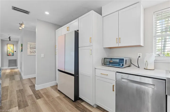 Kitchen featuring dishwasher, light countertops, white cabinetry, visible vents, and freestanding refrigerator  - Virtually Edited Image